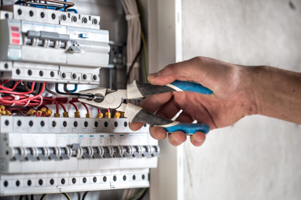 Man, an electrical technician working in a switchboard with fuses. Installation and connection of electrical equipment. Professional with tools in hand. concept of complex work, space for text.